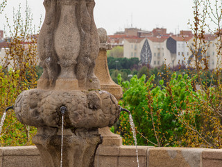 PIPE OF A WATER SOURCE ON THE TOLEDO BRIDGE OF MDRID. TO THE BACKGROUND MADRID RÍO AND BUILDINGS DECORATED WITH ECOLOGICAL REASONS FOR THE ANTONIO LOPEZ STREET LEVEL