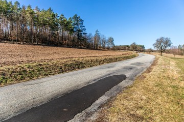 Old asphalt road near field. Czech landscape. Country road near the forest. Spring morning on country road.