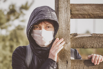 Woman in a disposable medical mask near a wooden fence. Coronavirus epidemic. Covid 19. Pandemic. Ukraine. Europe.
