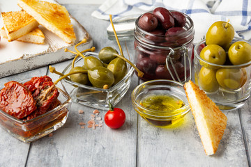 Italian antipasti, olives, capers, sun-dried tomatoes , olive oil, bread (ciabatta, baguette, croutons). Mediterranean assortment of delicious food, wine snacks