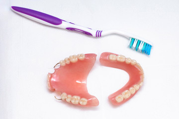 Dentures lie on a white background and a toothbrush, upper and lower jaw, top view. Dental prosthetics, care for removable dentures.