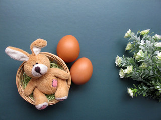 Easter holiday flat lay. Fluffy toy rabbit in a nest with flowers and eggs on a green background. Copy space for your text