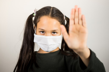 Cute latin girl with protective mask, makes the stop gesture with his hand on a white background