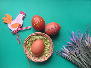 Easter holiday flat lay. Eggs in a nest, flowers and a decorative wooden chicken on a green background. Copy space for your text
