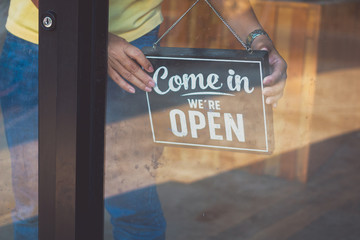 Woman Holding up a shop sign saying: Come in, We're Open.