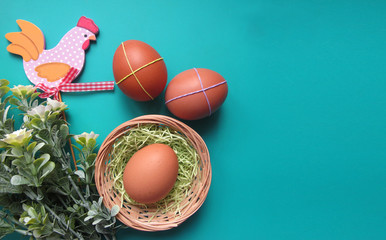 Fototapeta na wymiar Easter holiday flat lay. Eggs in a nest, flowers and a decorative wooden chicken on a green background. Copy space for your text