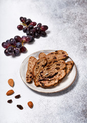 Sliced rusk fruit bread on a plate with red grapes, rosins and almond nuts. Homemade healthy food concept. Selective focus. Copy space.