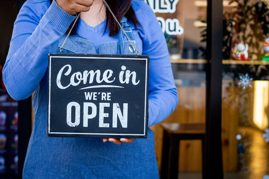 Woman Holding Up A Shop Sign Saying:Come In We're Open