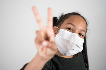 Portrait of girl with prevention mask who smiles and shows the sign of v in victory and hope against the coronavirus infection. Covid 19 hope concept.