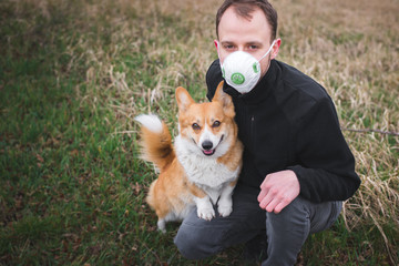 a man on a walk with a corgi dog wearing a face mask and during coronavirus pandemia