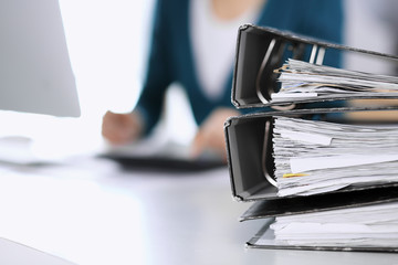 Binders with papers are waiting to be processed by business woman or bookkeeper working at the desk...