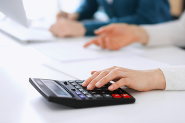 Accountant checking financial statement or counting by calculator income for tax form, hands closeup. Business woman sitting and working with colleague at the desk in office. Tax and Audit concept