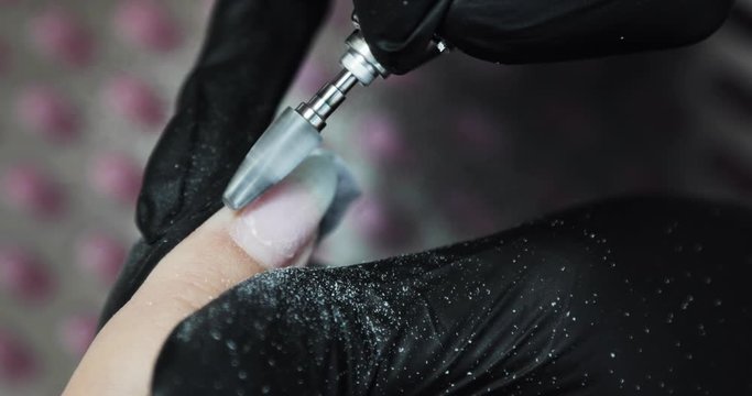 Manicure master in gloves removes nail polish gel shellac from woman's nails using electric drill machine, hands closeup. Hardware manicure in beauty salon.