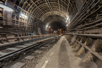 duble-track reinforced concrete tunnel of the metro line.One of the railway lines turns of the right.The light is on.Electric high-voltage cables run along the walls of the tunnel