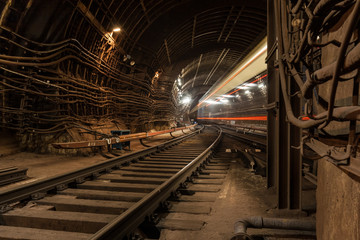 A passing train the lights of the metro tunnel.At the intersection of two metro lines.Goes into the tunnel.With red lines