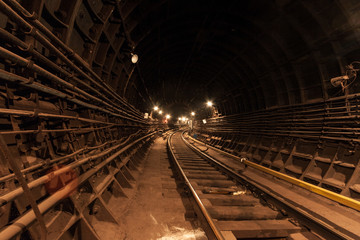 Fototapeta na wymiar A lighted reinforced concrete subway tunnel, cable routes are laid, the railroad tracks turn left. In front of them are iron vertical boxes of automatics.