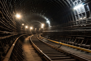 A lighted reinforced concrete subway tunnel, cable routes are laid, the railroad tracks turn left....