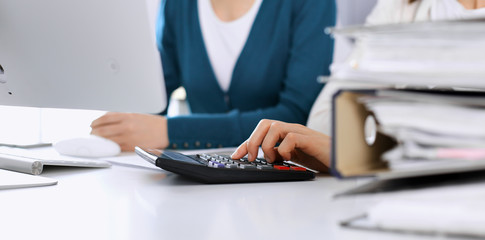 Accountant checking financial statement or counting by calculator income for tax form, hands closeup. Business woman sitting and working with colleague at the desk in office. Tax and Audit concept