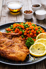 Schnitzel with boiled carrot and peas on wooden background