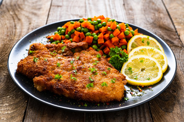 Schnitzel with boiled carrot and peas on wooden background