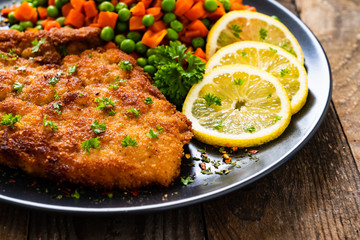 Schnitzel with boiled carrot and peas on wooden background