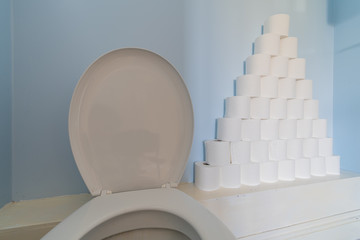 A huge pile of toilet paper stacked up next to a toilet