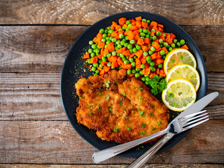 Schnitzel with boiled carrot and peas on wooden background