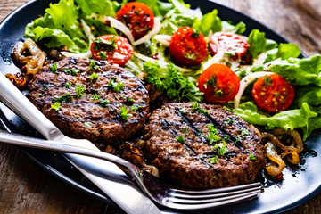 Barbecue steaks with vegetables on wooden background