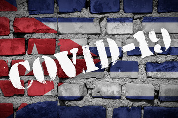 Flag of Cuba on the brick wall with sprayed stencil COVID-19 on it. 2019 - 2020 Novel Coronavirus...