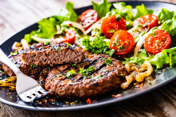 Barbecue steaks with vegetables on wooden background