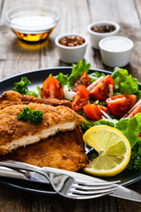 Pork chops with lemon and vegetable salad on wooden background