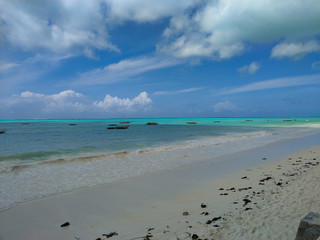 Fototapeta na wymiar Traumkulisse, Fernweh und Karibik feeling am weißen Strand auf Sansibar, mit türkisen Meer und Schäfchenwolken im Hintergrund