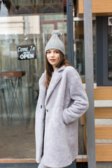 Street style. Caucasian girl posing in front of a carousel. Winter or autumn clothes. Pastel colors. Fun and smile. Merry-go-round.