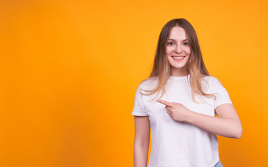 Obraz premium Smiling happy girl shows aside on a yellow background.