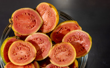 guava fruits (Psidium guajava) in halves in bowl on dark background