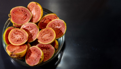 guava fruits (Psidium guajava) in halves in bowl on dark background