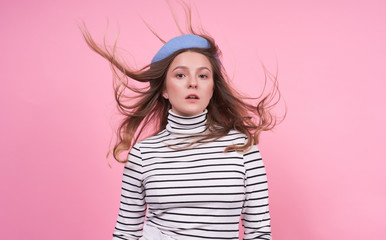 Cool charming girl with flying hair in a blue beret on a pink background.