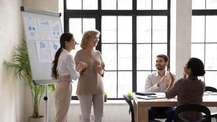 Smiling middle-aged businesswoman handshake excited millennial female employee congratulate with...