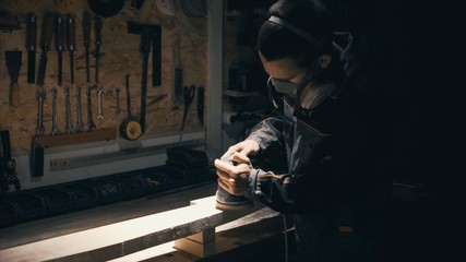 Man polishing solid wood, joiner labouring in mask for safety