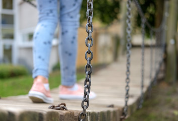 Junges, schlankes Mädchen auf einem Spielplatz zieht sich mit einem Tau auf ein Spielgerät balanciert auf einer Dschungelbrücke auf einem Spielplatz / selektiver Fokus, viel copy space