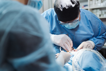 Doctors with surgical tools in hands making surgery in operation room. Health care or veterinary care concept.