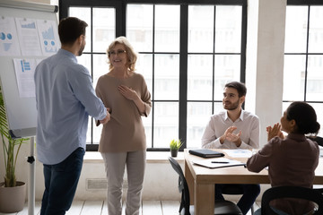 Male team leader handshake middle-aged female employee greeting with promotion at meeting in office, happy businessman shake hand of excited woman worker congratulate with job achievements