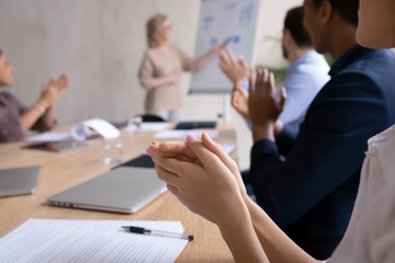 Close up of diverse businesspeople sit at desk at meeting clap hands greeting speaker or couch, excited multiracial colleagues applaud thanking leader or tutor for presentation at office briefing