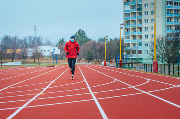 Fototapeta premium Runner wearing medical mask, Coronavirus pandemic Covid-19 in Europe. Sport, Active life in quarantine surgical sterilizing face mask protection. Outdoor run on athletics track in Corona Outbreak