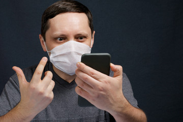 A man in a medical mask is talking on a smartphone, video conferencing. During a conversation, makes a gesture of indignation with his hand. Protection against infection.