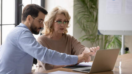Concentrated diverse colleagues sit at desk in office brainstorm discuss business ideas using...