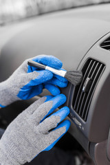 Car interior cleaning and detailing. Hands wearing gloves holding brush.
