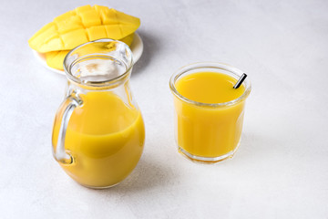 Glass and Decanter of Tasty Ripe Mango Juice and Ripe Sliced Mango on Light Gray Background Vitamin and Healthy Drink