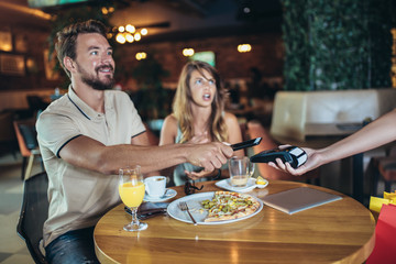 Happy couple using mobile phone and making contactless payment in a restaurant. S