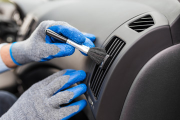 Professional car cleaning service. Man hands in protective gloves removing dust from air duct with soft brush.